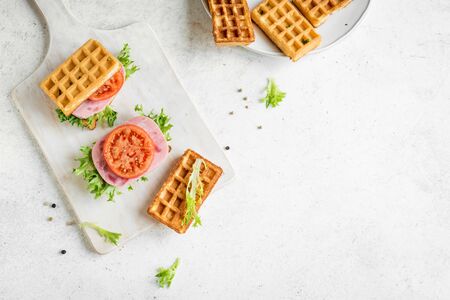 Savory waffle sandwich with ham and tomato for keto breakfast. Chaffle (cheese and egg waffle) sandwich on white, top view, copy space.の写真素材