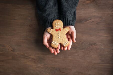 Hands holding Christmas gingerbread cookie, decorated gingerman on wooden background, top view, copy...