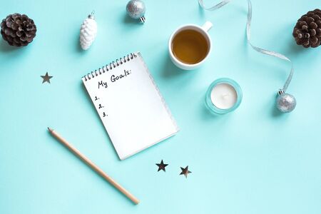 My Goals list written on paper with cup of tea, pencil and Christmas festive decor, flat lay on blue...