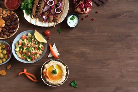 Middle Eastern Arabic food, dinner table. Meat kebab, hummus, tabbouleh salad, traditional sauces, olives, pita,  dates fruits, nuts, pomegranate. Set of Arabian meal, top view, copy space.の写真素材