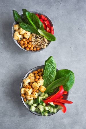 Fried Tofu Salad with Cucumbers, Fried Chickpeas, Leaves vegetables and Sesame Seeds. Balanced vegan colorful salad for healthy lunch in ceramic bowls, top view.の写真素材