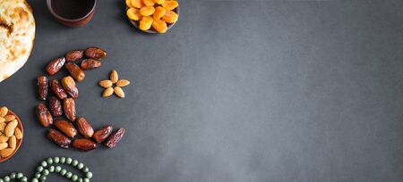 Muslim Ramadan Kareem with dates fruits arranged in shape of crescent moon, water and bread on black background, banner, copy space. Iftar party concept.の写真素材