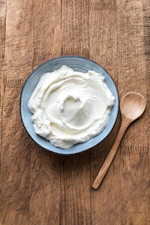 Natural Greek Yogurt in ceramic bowl on wooden background, top view. Fresh homemade organic plain yogurt or sour cream.の写真素材