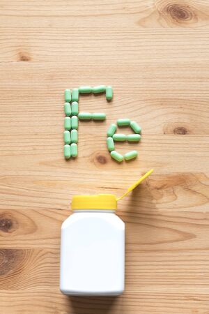 Green pills forming shape to Fe alphabet on woodenの写真素材