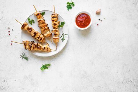 Chicken skewers or kebabs on white table, top view, copy space. Grilled meat pork, chicken or turkey shish kebab with tomato sauce, herbs and spices, barbeque meal.の写真素材