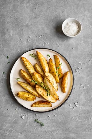 Roasted potato wedges with herbs and sea salt on plate, top view, copy space. Homemade oven baked potato snacks and sour cream sauce.の写真素材