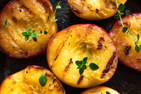 Grilled Peaches with Thyme, Honey close up. Homemade bbq roasted peaches or nectarines, rustic summer or autumn dessert.の写真素材