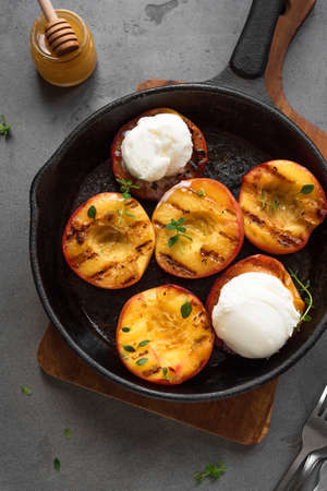 Grilled Peaches with Thyme, Honey and scoop of Vanilla Ice Cream in black pan, top view. Homemade bbq roasted peaches or nectarines, rustic summer dessert.の写真素材
