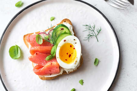 Healthy open salmon sandwich with cream cheese, soft egg, veggies and greens. Delicious protein fish sandwich for breakfast or brunch, top view, copy space.の写真素材