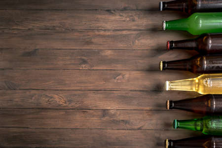 Assortment of beer bottles on dark wooden background, top view, copy space. Fresh cold beer for choice. Various sorts of beer.の写真素材