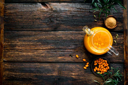 Tea with sea buckthorn berries in glass teapot on rustic wooden background, top view, copy space. Seasonal autumn sea-buckthorn spicy tea.の写真素材