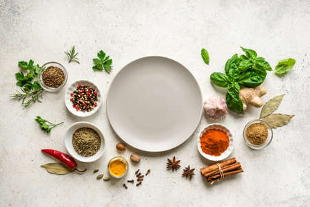 Various Spices, Herbs and Condiments around plate on white stone table, top view, copy space. Healthy cooking, indian food background.の写真素材