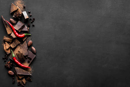 Dark Chocolate Background. Chocolate pieces, cacao powder, hot chili peppers and spices on black...