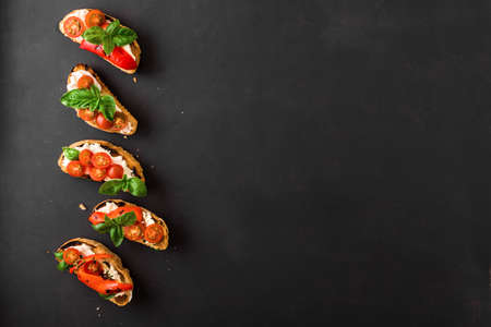 Bruschetta sandwiches with tomatoes, cream cheese, grilled paprika and basil on dark background, top view, copy space. Traditional italian snack - grilled bruschetta toasts.の写真素材