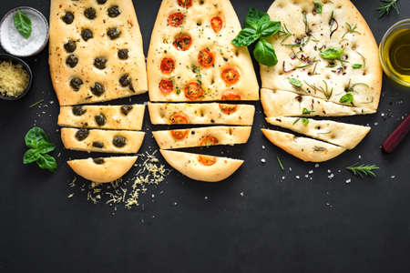 Italian Focaccia Bread with various fillings on black background. Fresh baked focaccia with tomatoes, olives, garlic and herbs, top view, copy space.の写真素材