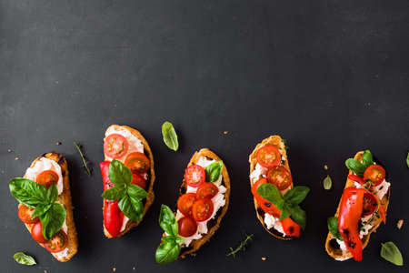 Bruschetta sandwiches with tomatoes, cream cheese, grilled paprika and basil on dark background, top view, copy space. Traditional italian snack - grilled bruschetta toasts.の写真素材