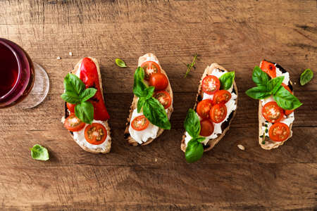 Bruschetta sandwiches with tomatoes, cream cheese, grilled paprika and basil on wooden background, top view. Traditional italian snack for wine - grilled bruschetta toasts.の写真素材