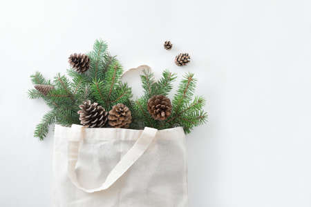 Christmas composition. Eco bag with Christmas tree branches and pine cones on white background....