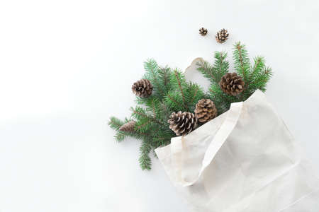 Christmas composition. Eco bag with Christmas tree branches and pine cones on white background....