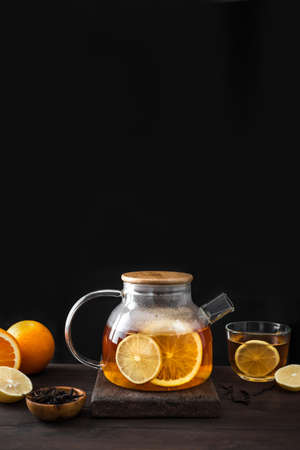 Citrus tea with lemon, oranges in modern glass teapot on dark wooden table, copy space. Fruit tea....