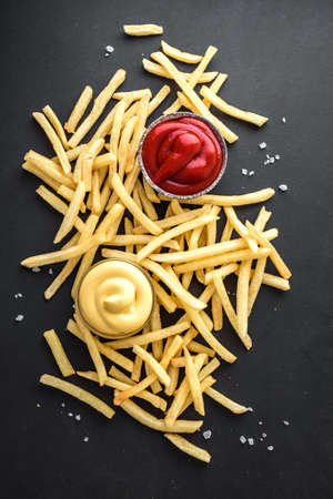 French fries on black board with ketchup and cheese sauce, top view, copy space. Homemade french...