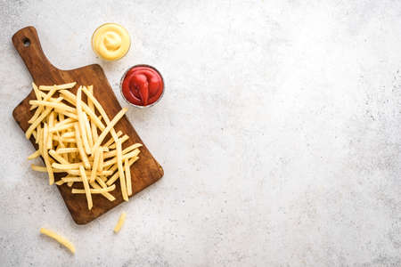 French fries on board with ketchup and cheese sauce, top view, copy space. Homemade french fries on...