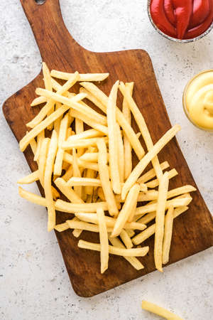 French fries on board with ketchup and cheese sauce, top view, copy space. Homemade french fries on...