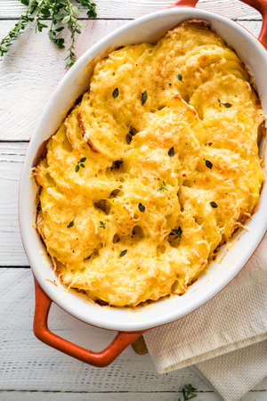 Potato gratin. Fresh baked cheesy potato casserole on white wooden table, top view, close up.の写真素材