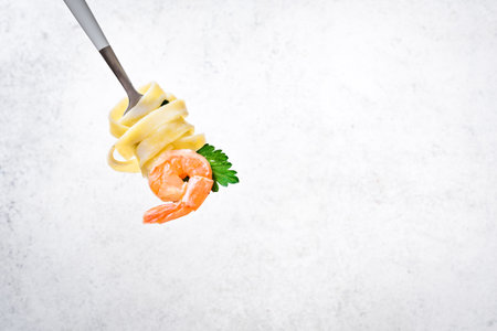 Fork with pasta and shrimp on white background, copy space. Fettuccine pasta with cream alfredo sauce and shrimp on fork close up.の写真素材
