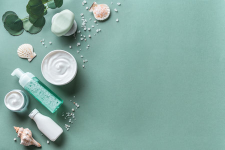 Sea mineral cosmetic products. Skin care, body treatment products, eucalyptus leaves, sea salt and shells on green background, top view, copy space. Spa and natural skin care concept.の写真素材