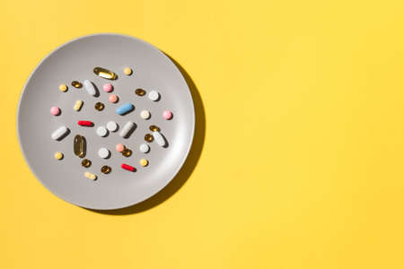 Many various vitamin pills and supplements as food on gray plate, yellow background. Nutritional supplements dosage concept. Taking medication. Pills instead of food.の写真素材