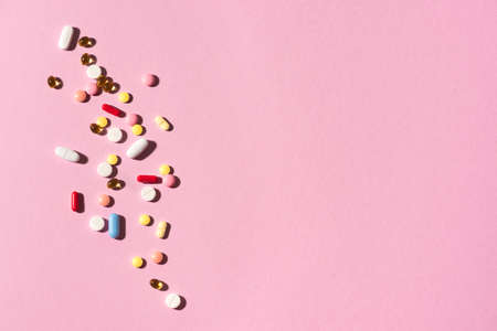 Multicolored tablets, pills, capsules on pink background, copy space. Heap of assorted various medicine tablets and pills, vitamin and nutritional supplements concept.の写真素材