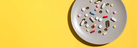 Many various vitamin pills and supplements as food on gray plate, yellow background. Nutritional...