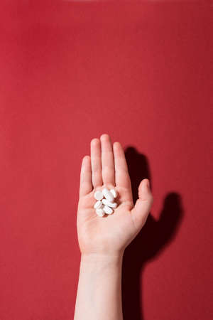 Medicine pills, vitamins, nutritional supplements on hand, red background, copy space. Medical concept.の写真素材