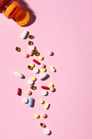 Multicolored tablets, pills, capsules falling from plastic bottle on pink background. Heap of...