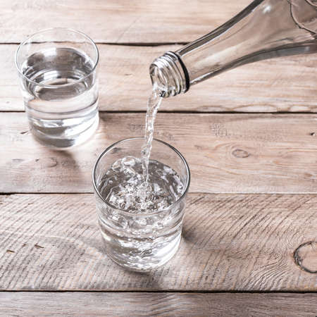 Water pouring into glass. Glass of water on wooden table, selective focus. Clear purified water for...
