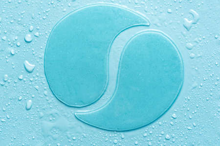 Hydrogel blue eye patches on blue background with water drops close up. Cosmetic moisturizing under...