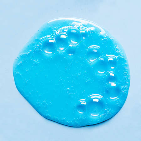Blue shampoo or shower gel sample puddle on blue background. Blue gel cosmetic product with bubbles.