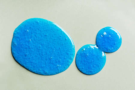 Blue shampoo or shower gel sample drops on gray background. Blue gel cosmetic product with bubbles.