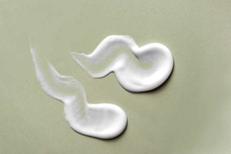Cosmetic cream drops texture smudged on green background, top view. White swatches of skin care...