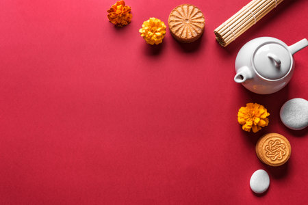 Mid Autumn festival concept. Chinese moon cake, tea and flowers on red background and bamboo mat, top view, copy space.