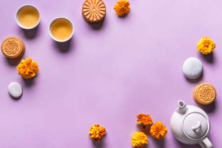 Mid Autumn festival concept. Chinese moon cake, tea and flowers on purple background, copy space.