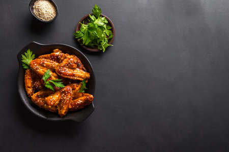 Teriyaki chicken wings with sesame and greens on black background, top view, copy space. Asian style meal - roasted chicken wings with teriyaki sauce.の写真素材