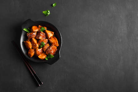Teriyaki chicken pieces with sesame and greens on black background, copy space. Asian style meal - roasted chicken fillet with teriyaki sauce.の写真素材