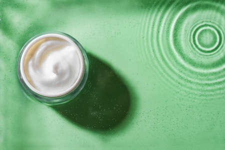 Jar of cosmetic cream on clear green water background, top view, copy space. Moisturizing organic beauty cream. Hydrating natural skin care and spa concept.の写真素材