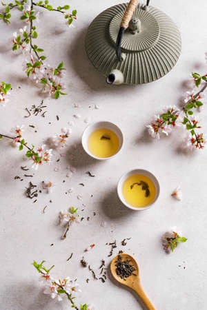 Green Tea and Cherry Blossom on white stone table. Japanese cast iron teapot and cups, Asian green tea composition with sakura bloom and petals.の写真素材