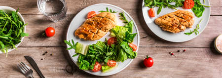 Grilled Chicken Salad with fresh vegetables and greens on wooden table. Roasted Chicken Breast, green lettuce, arugula, tomatoes salad for healthy lunch, banner.の写真素材