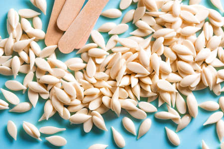 Granular film wax bean granules and wooden spatula on blue background close up. Hair removal,...