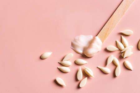 Melted and granular film wax beans and wooden spatula for depilation. Natural hair, removal beauty concept, white pearl wax on pink background, copy space.の写真素材