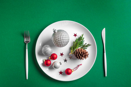 Creative Christmas Table Setting. Festive balls and decor on white plate on green background, top view, copy space. Christmas dinner, party design, menu concept.の写真素材